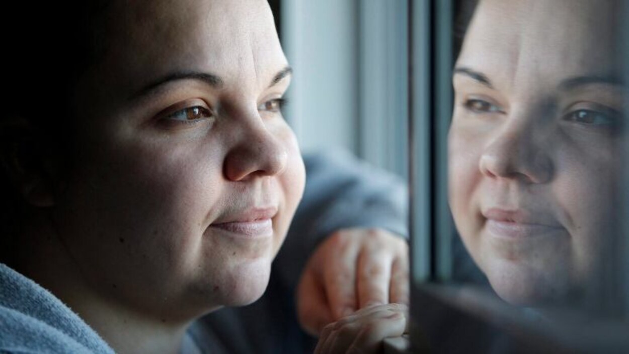Jessica Reid regarde par une fenêtre, sur laquelle on peut voir le reflet de son visage.