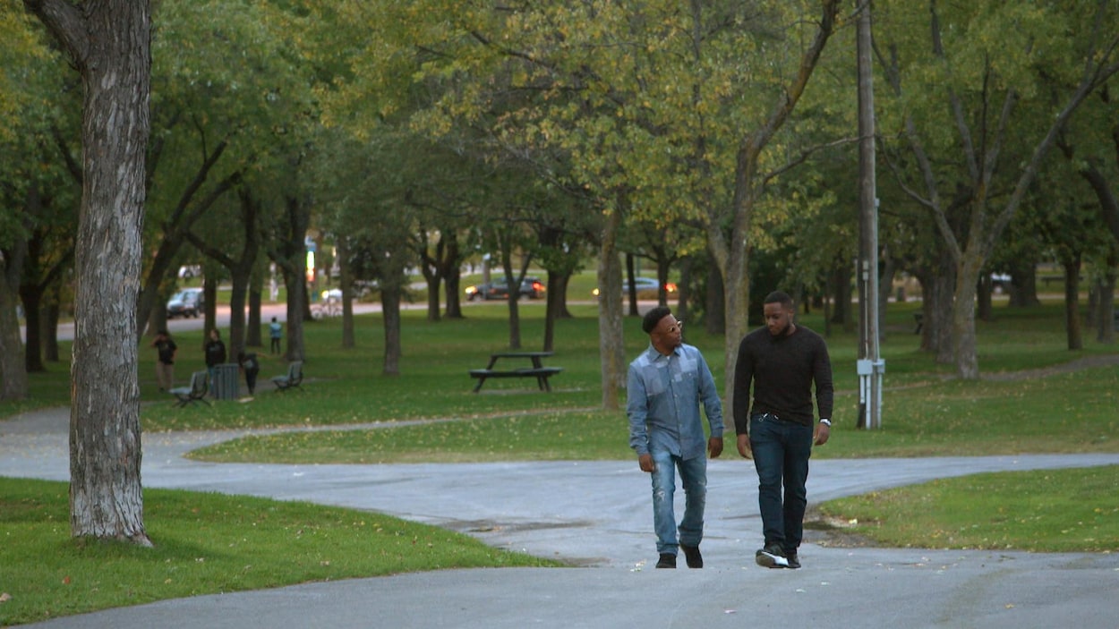 Deux jeunes hommes portant des chandails à manche longue et des pantalons marchent dans un parc presque désert. Les deux Noirs entretiennent une conversation.