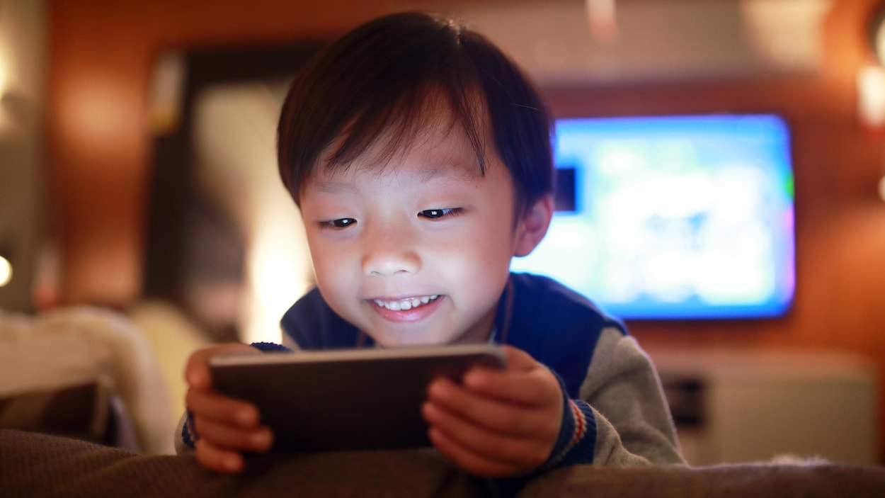 Un jeune garçon regarde l'écran d'un téléphone.