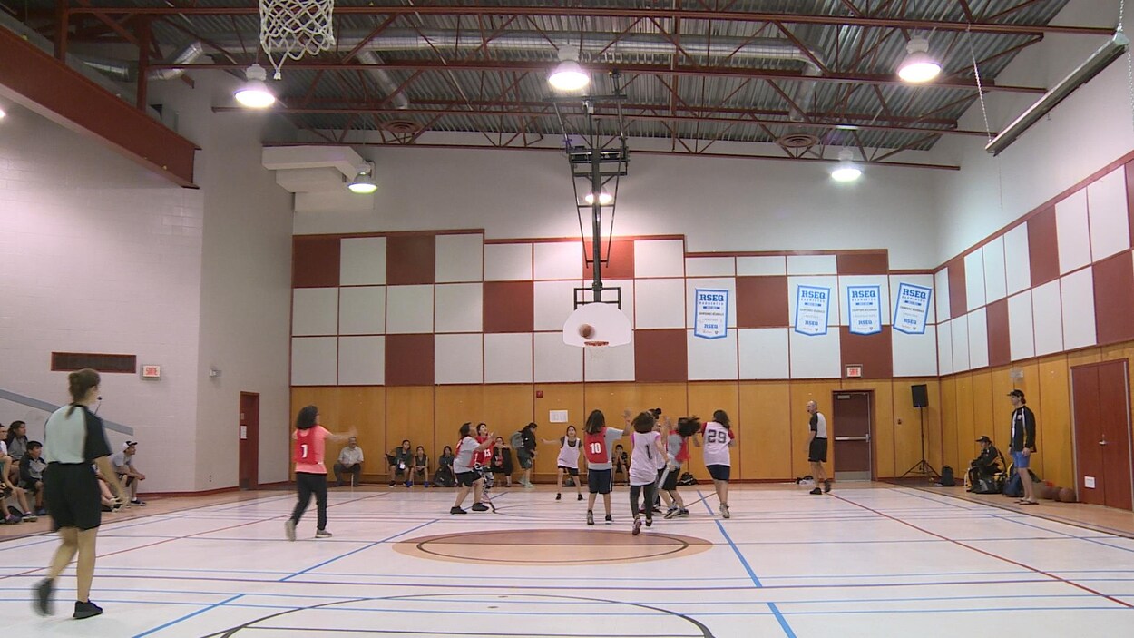 Des jeunes avec des dossards jouent au basketball dans un gymnase.