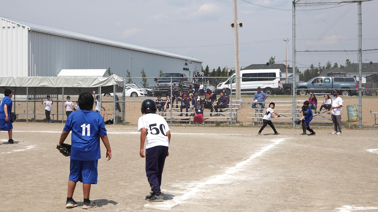 Des jeunes jouent au baseball devant quelques personnes assises dans des gradins.