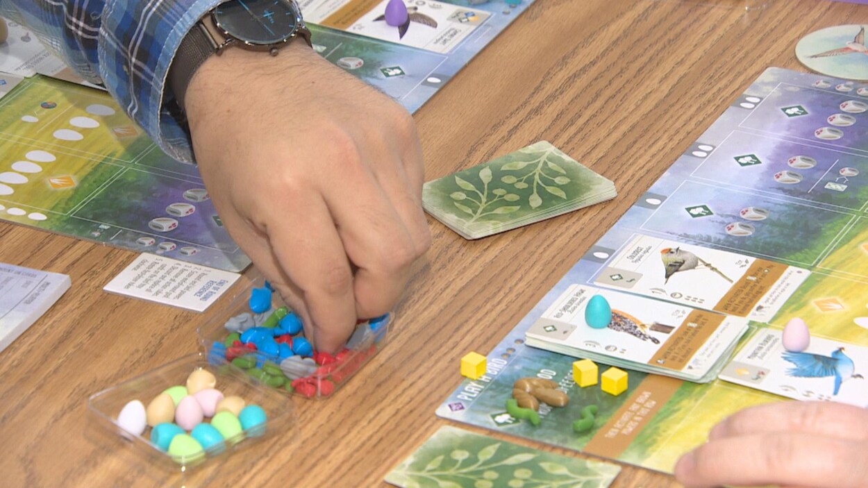 La main d'un joueur pioche un jeton dans une petite boîte en plastique faisant partie d'un jeu de société.