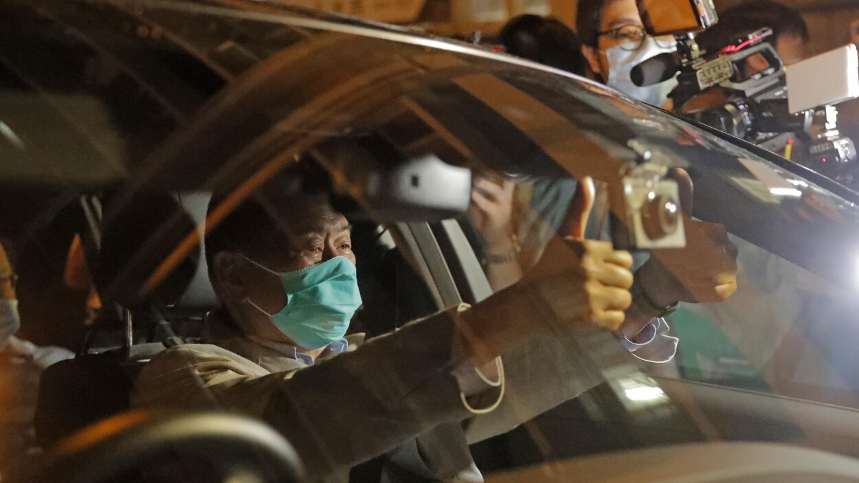 Jimmy Lai, assis dans voiture, masqué, montre ses deux pouces en l'air.