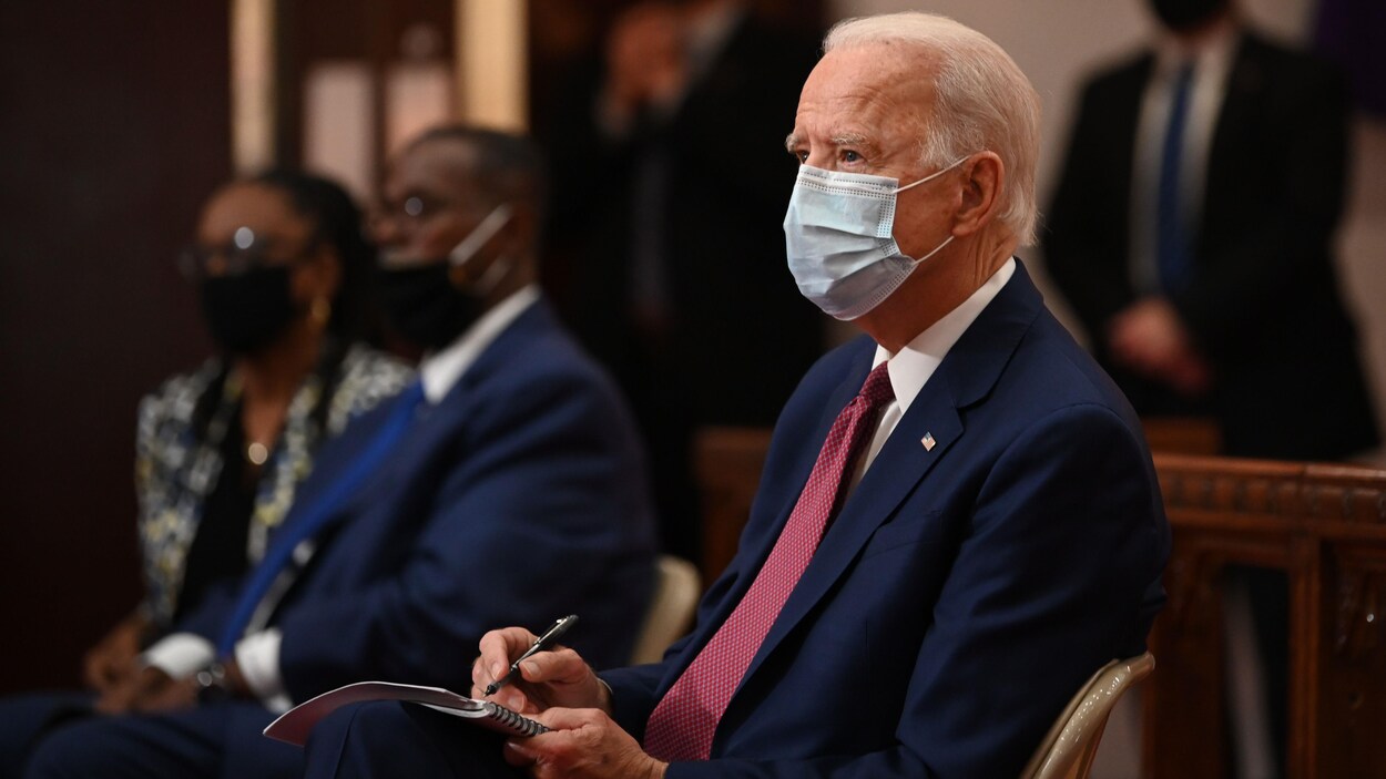 Le candidat démocrate Joe Biden portant un masque avec quelques personnes en arrière-plan.