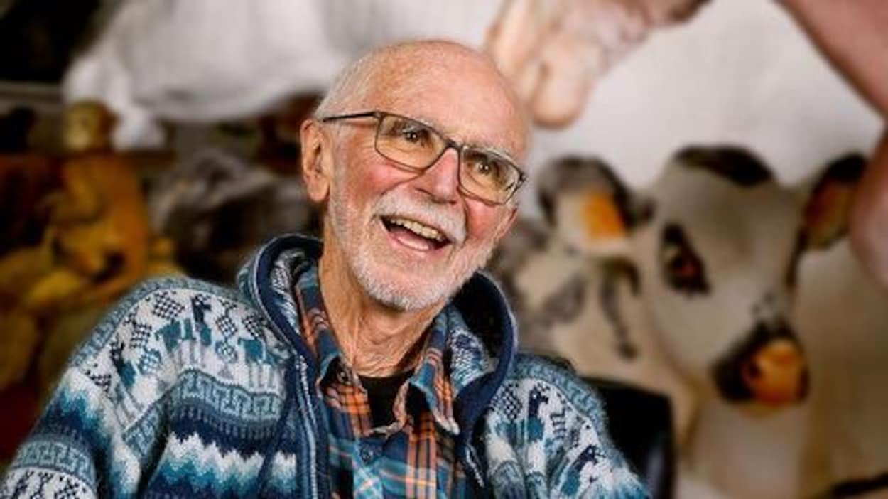 Joe Fafard assi sur une chaise, entouré par ses oeuvres, sourit à la caméra.
