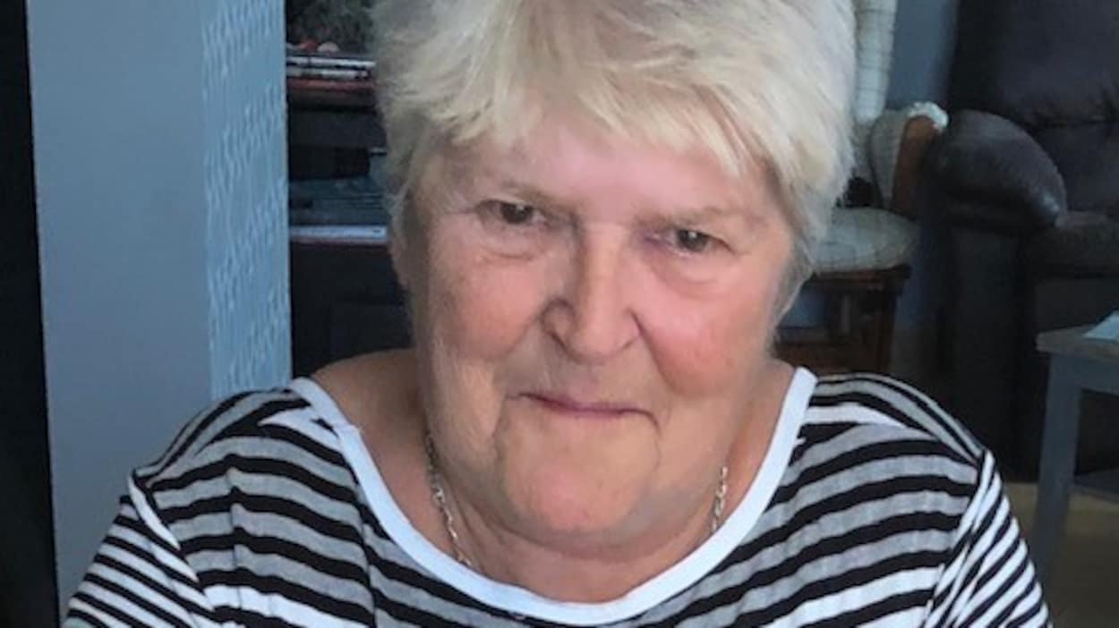 Une dame âgée dans son salon. elle porte un chandail avec des rayures.