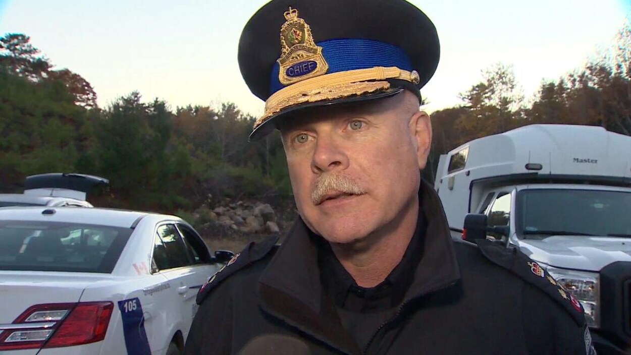 John Collyer en uniforme de policier, coiffé de son képi.