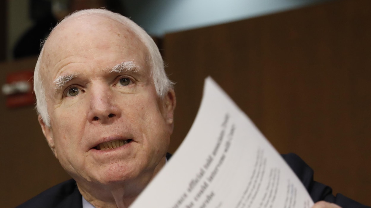 Le sénateur républicain John McCain regarde droit devant lui et tient un document dans sa main gauche.