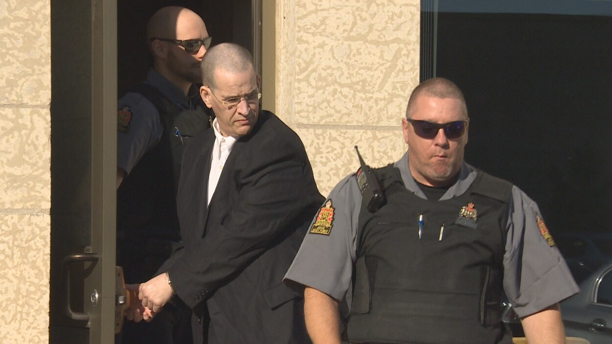John Strang quitte menotté la Cour du Banc de la Reine à Regina entouré de deux policiers portant un gilet pare-balles.