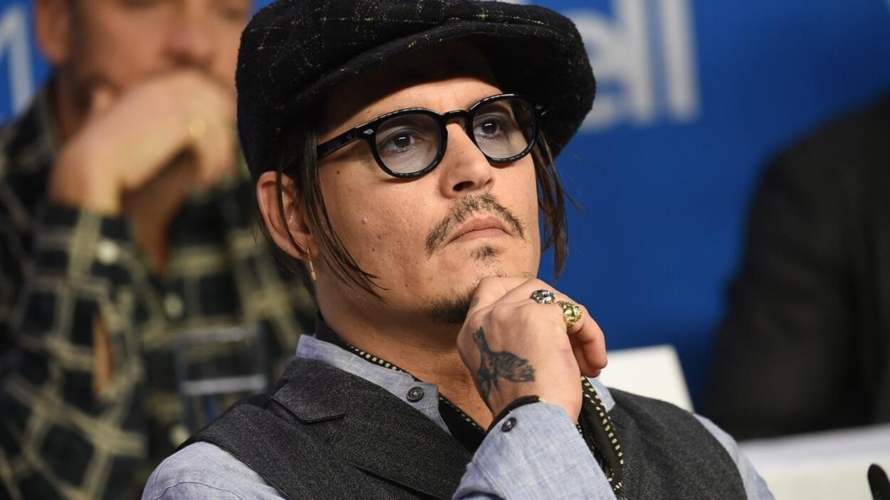 Johnny Depp, portant des lunettes, est assis durant une conférence de presse.