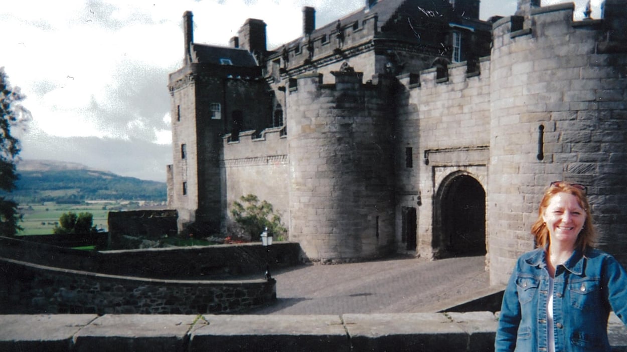 Une femme pose devant un château médiéval.