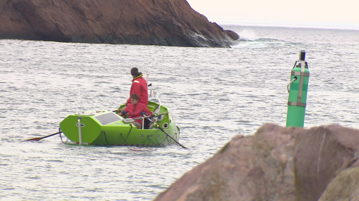 Deux hommes rament hors d'une baie rocheuse.