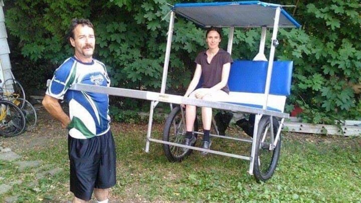 Joseph-Hugues Bélanger se tient debout à côté d'un pousse-pousse à bord duquel est assise une femme.