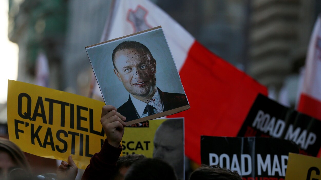 Un manifestant tient une photo du visage de Joseph Muscat, éclaboussé de sang.