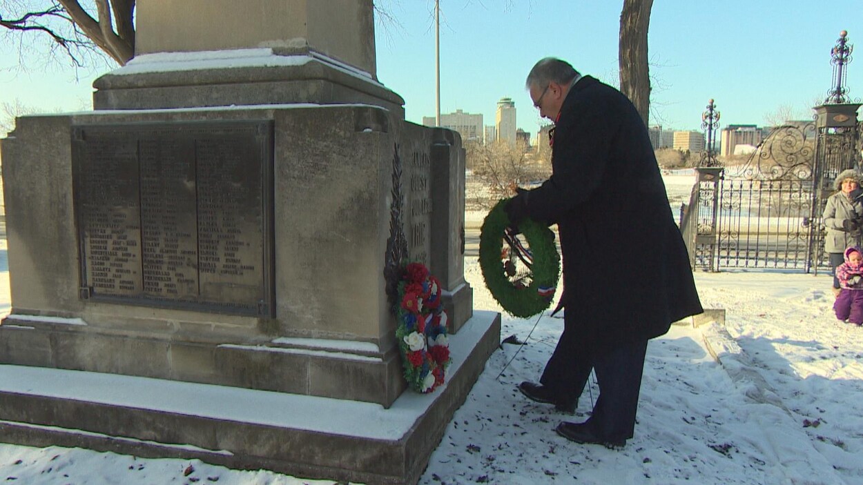 Un homme dépose une couronne de fleurs au pied d'un monument commémoratif.