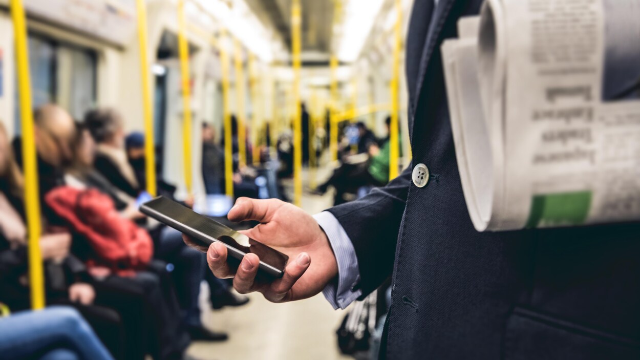 Un homme transportant un journal consulte un téléphone intelligent dans le métro.
