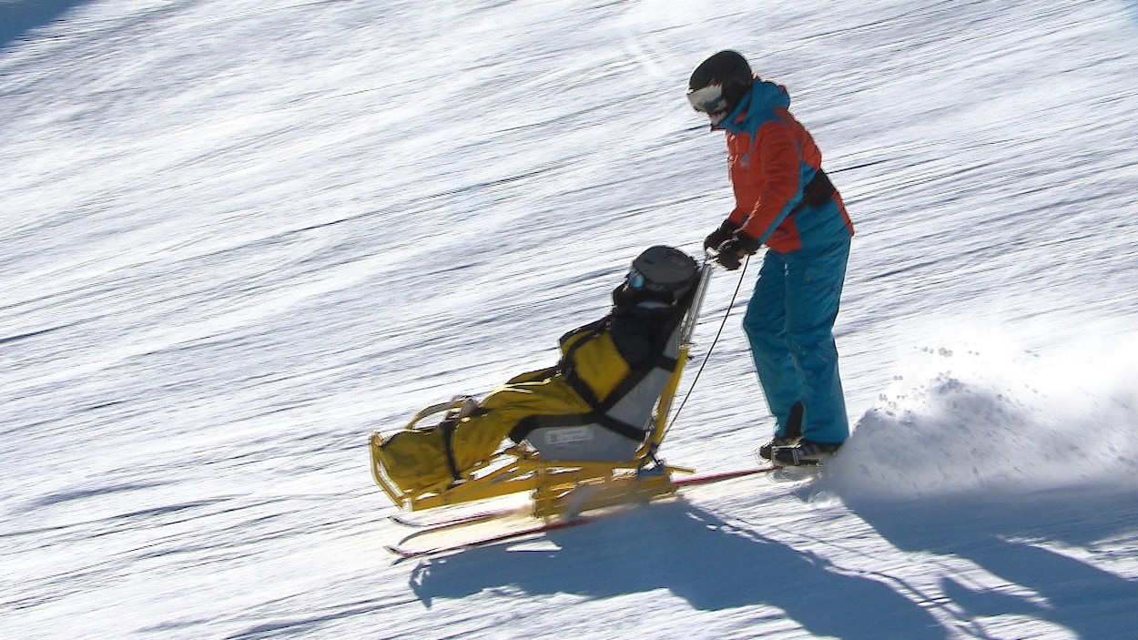 Un homme dévale une piste de ski une chaise de ski adaptée portant une personne handicapée.