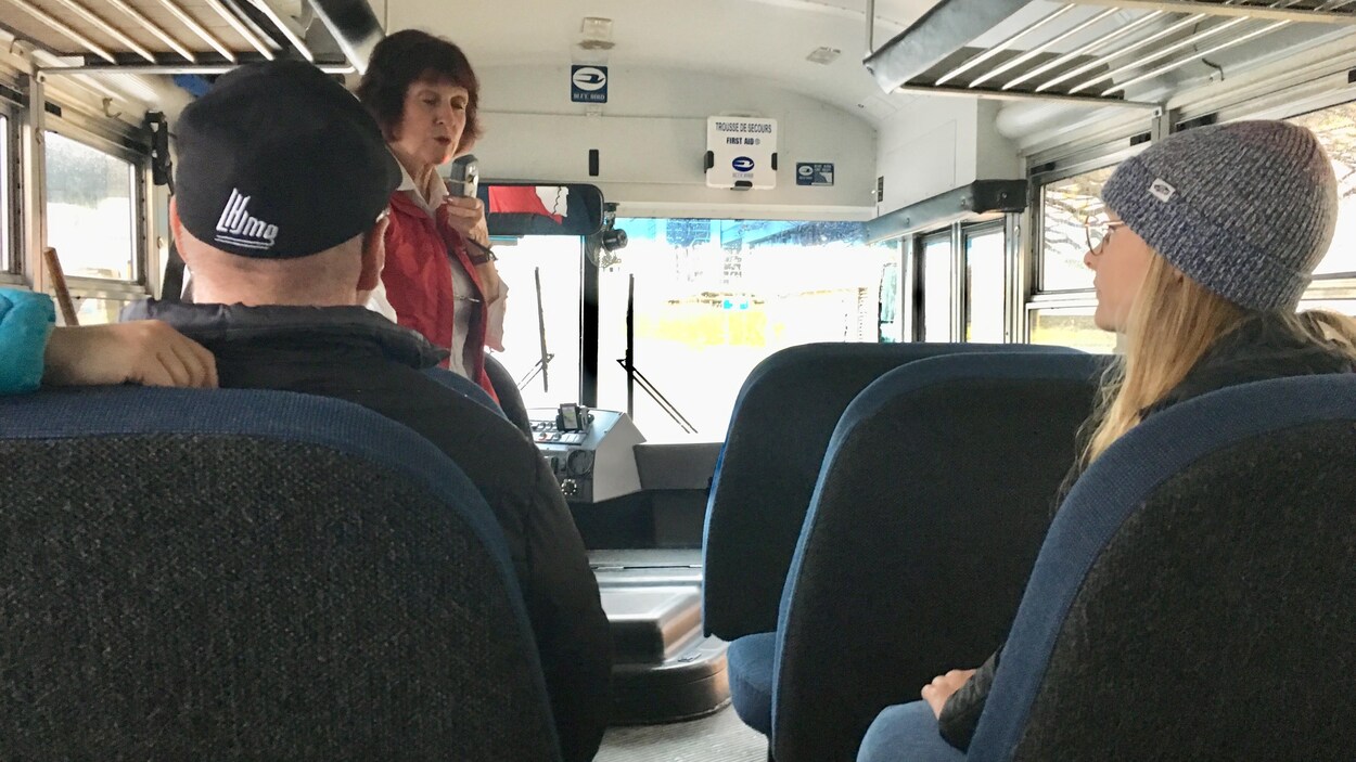 Un autobus scolaire avec une guide, une fille blonde à droite et un homme rasé portant une casquette à gauche.