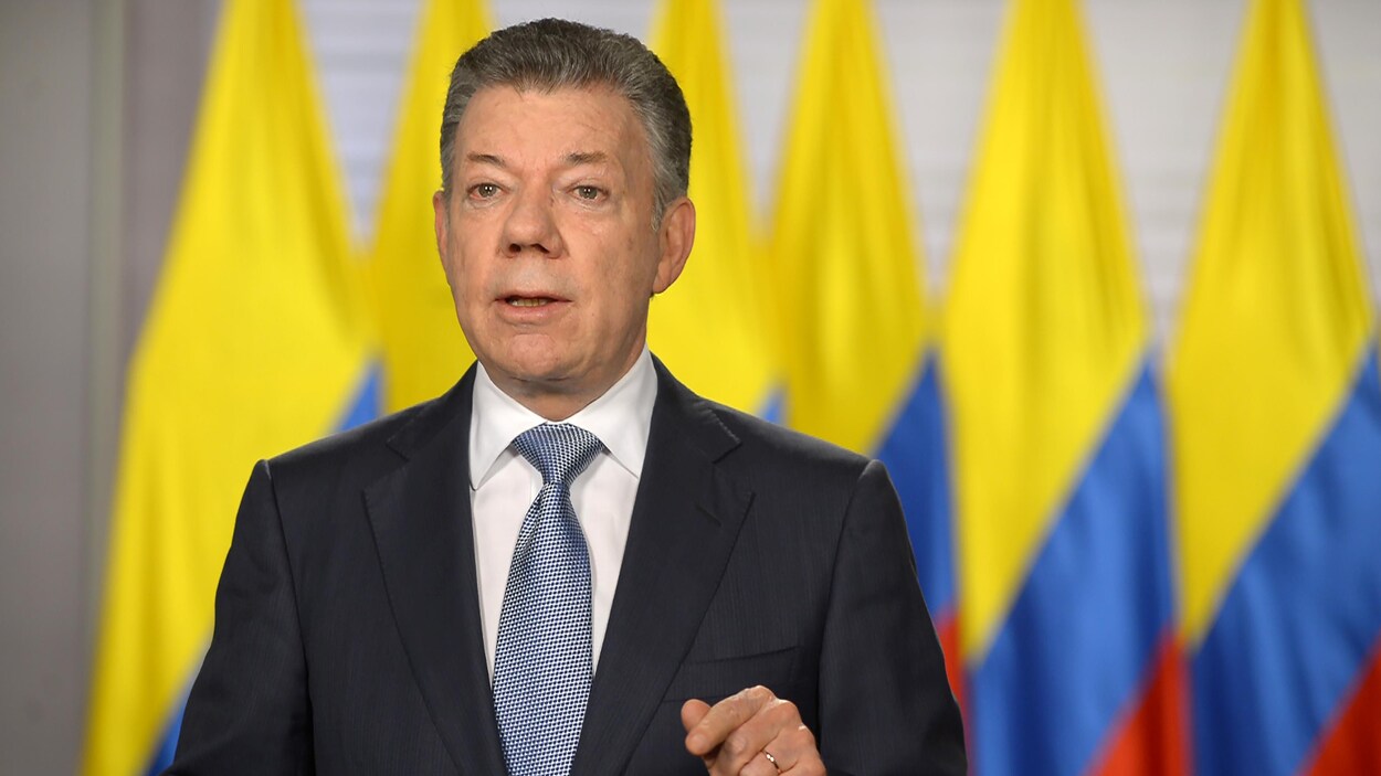Les cheveux poivre et sel, le président colombien Juan Manuel Santos parle devant des drapeaux colombiens.