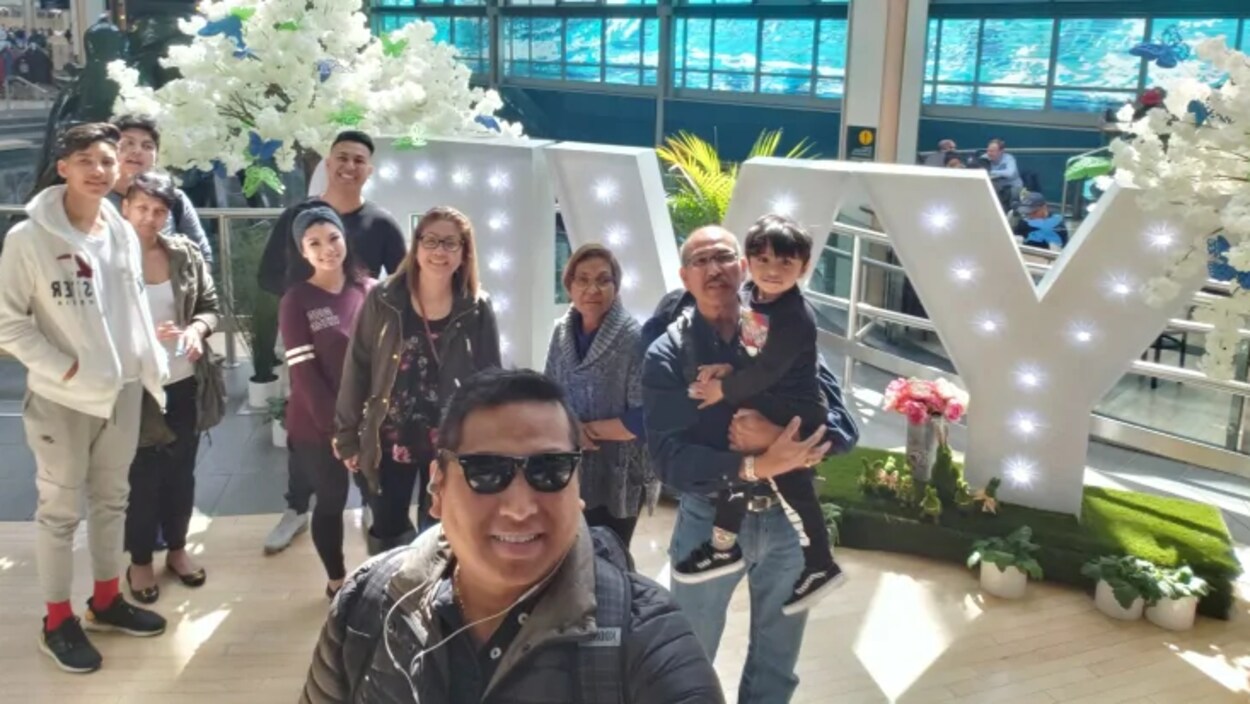 Une famille de 10 membres se prennent en photo dans un aéroport.