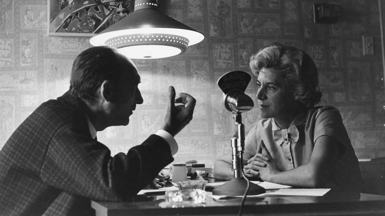 Judith Jasmin et Jean Vilar discutent autour d'une table. Judith Jasmin et Jean Vilar discutent autour d'une table.