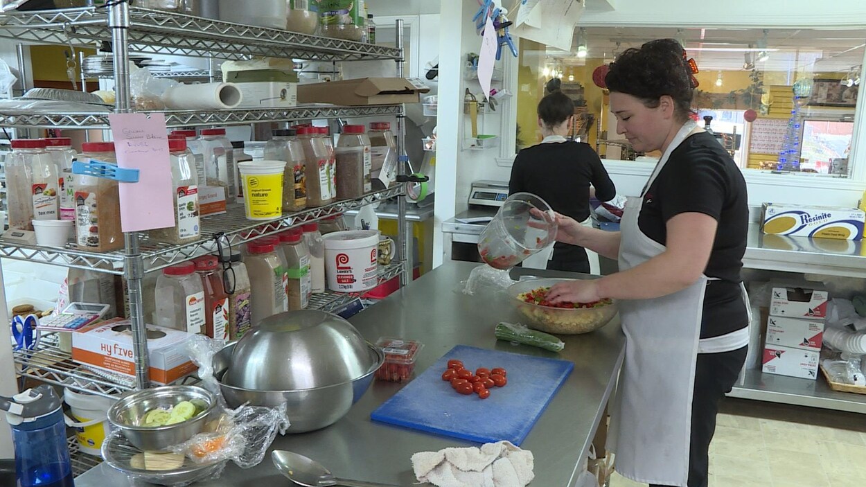 Une femme prépare une salade dans une cuisine industrielle.