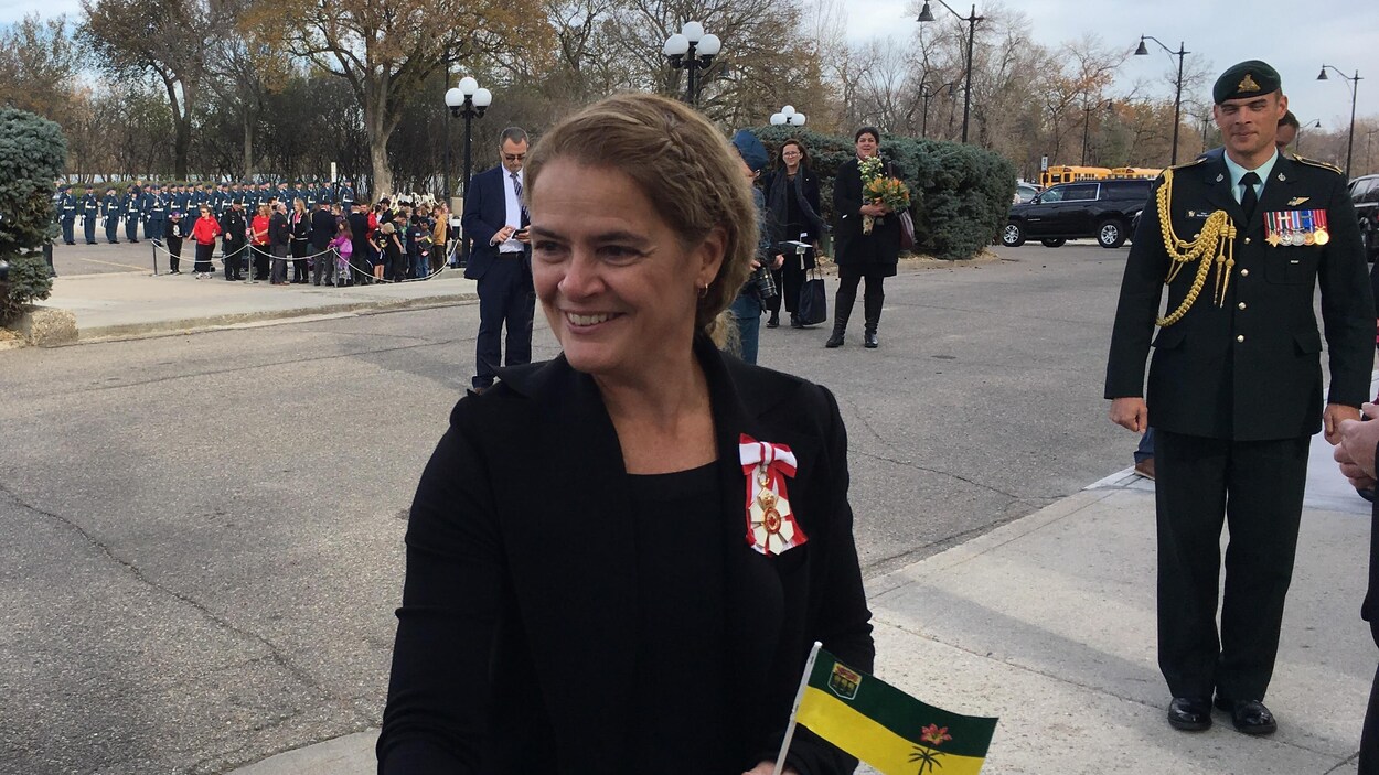 Julie Payette sert la main d'une femme en tenant dans l'autre main un drapeau de la Saskatchewan. Julie Payette sert la main d'une femme en tenant dans l'autre main un drapeau de la Saskatchewan.
