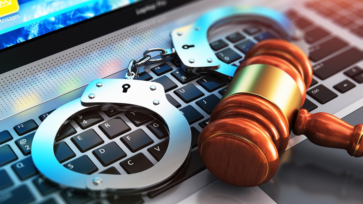 Sur un clavier d'ordinateur repose des menottes ainsi qu'un maillet représentant la justice. Sur un clavier d'ordinateur repose des menottes ainsi qu'un maillet représentant la justice.