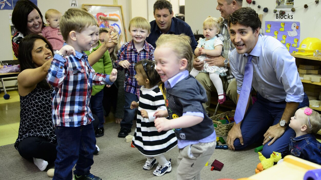 Justin Trudeau est agenouillé devant des enfants, dont certains sont accompagnés par un parent.