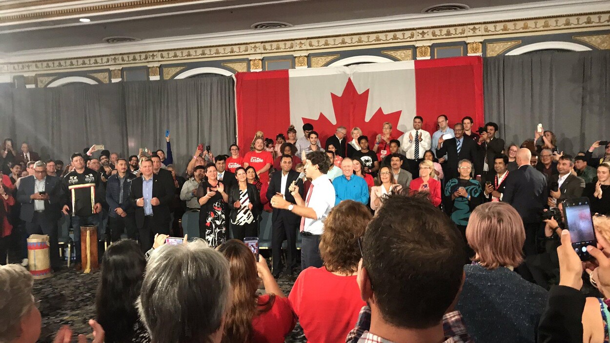 Justin Trudeau un micro à la main prend la parole entourée d'une foule dans une grande salle.