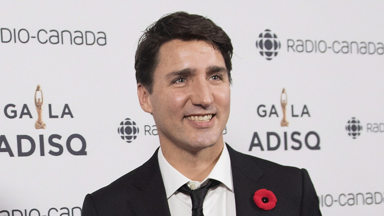 Justin Trudeau à son arrivée au Gala de l'ADISQ, souriant sur le tapis rouge, vêtu d'un sobre veston noir sur une chemise blanche et une cravate noire.