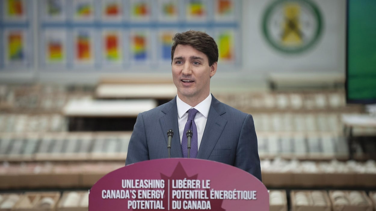 Justin Trudeau se tient sur un podium, devant un lutrin sur lequel est écrit, en français et en anglais : «Libérer le potentiel énergétique du Canada»