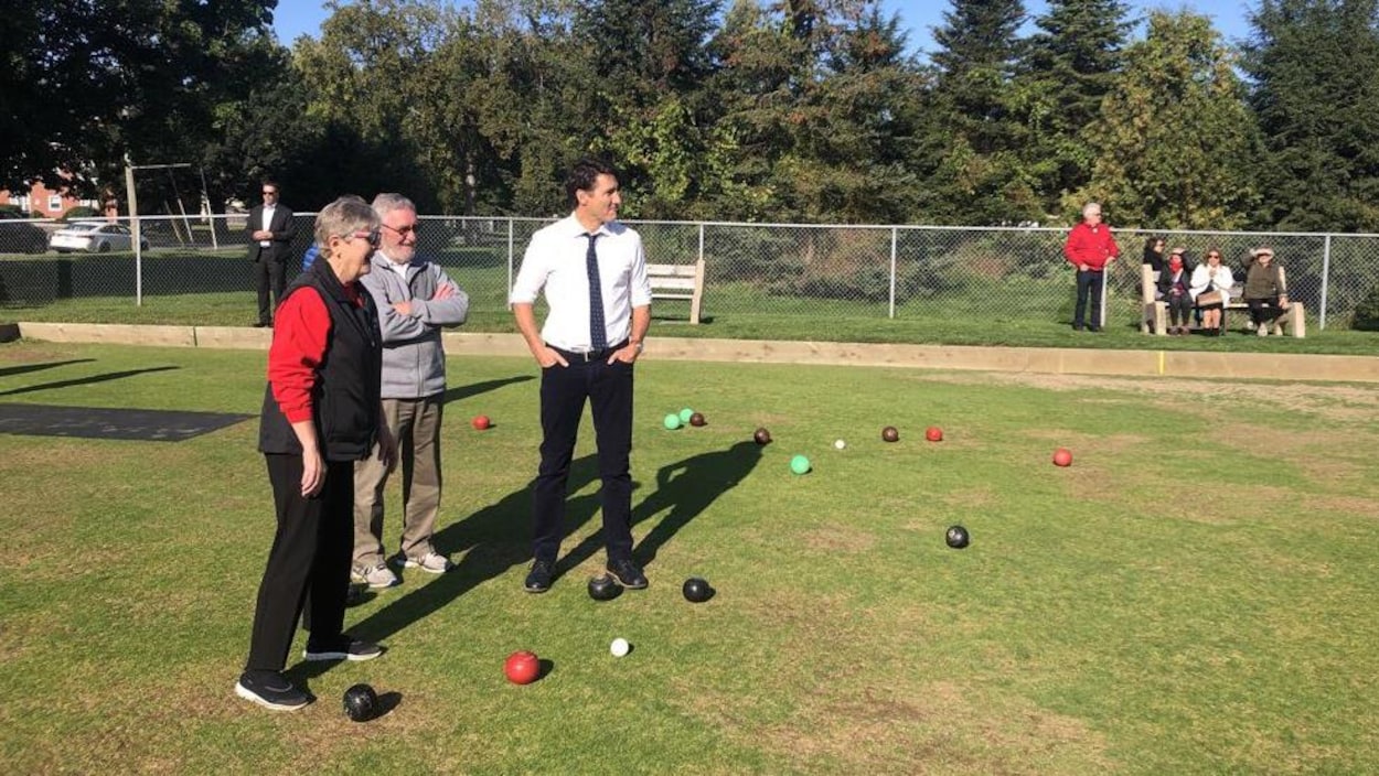 M. Trudeau regarde devant lui sur un terrain gazonné, en compagnie de deux personnes âgées.