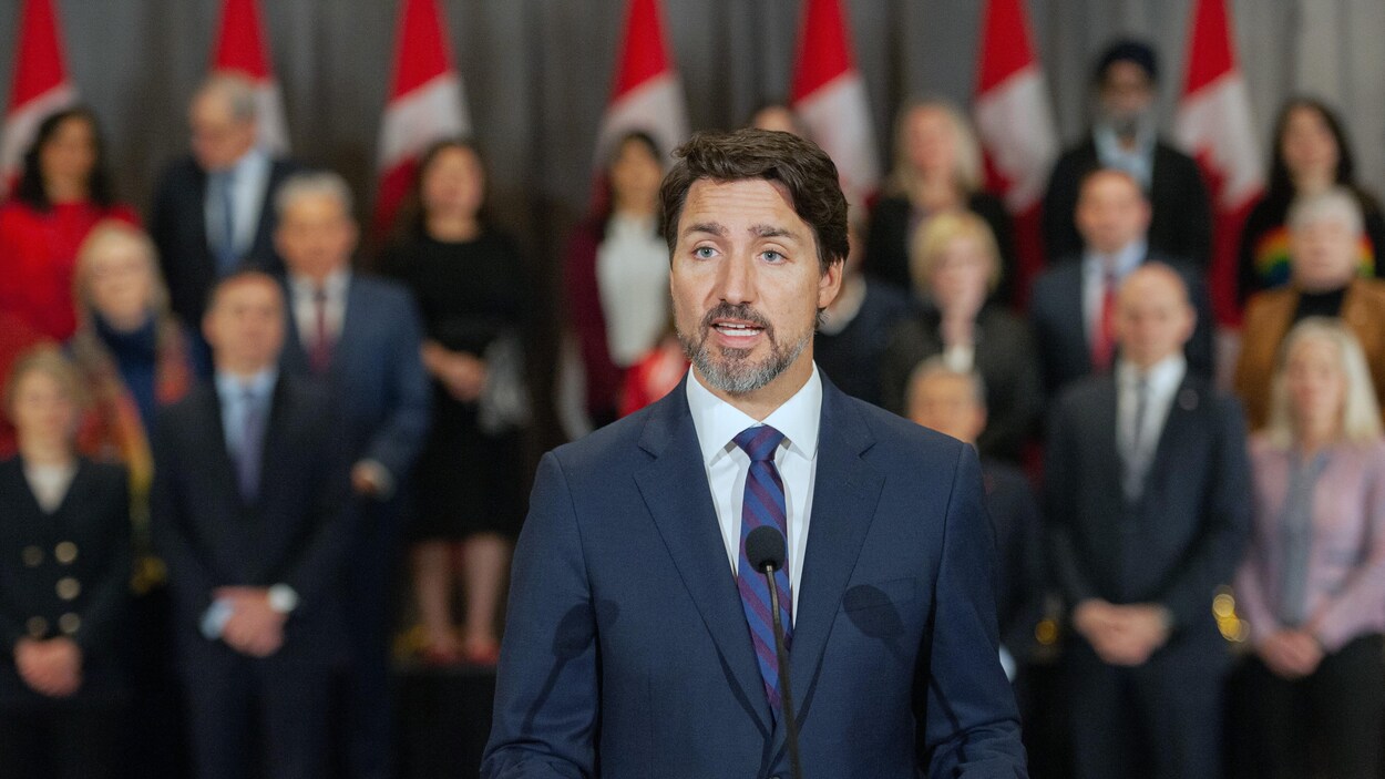 Justin Trudeau parle en conférence de presse. Ses ministres se tiennent debout derrière lui.