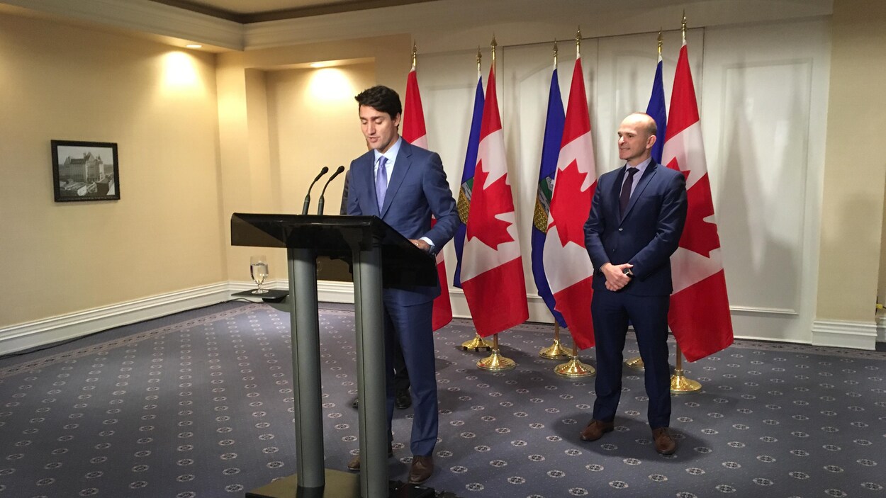 Justin Trudeau et un autre homme en conférence de presse devant des drapeaux du Canada et de l'Alberta. Justin Trudeau et un autre homme en conférence de presse devant des drapeaux du Canada et de l'Alberta.