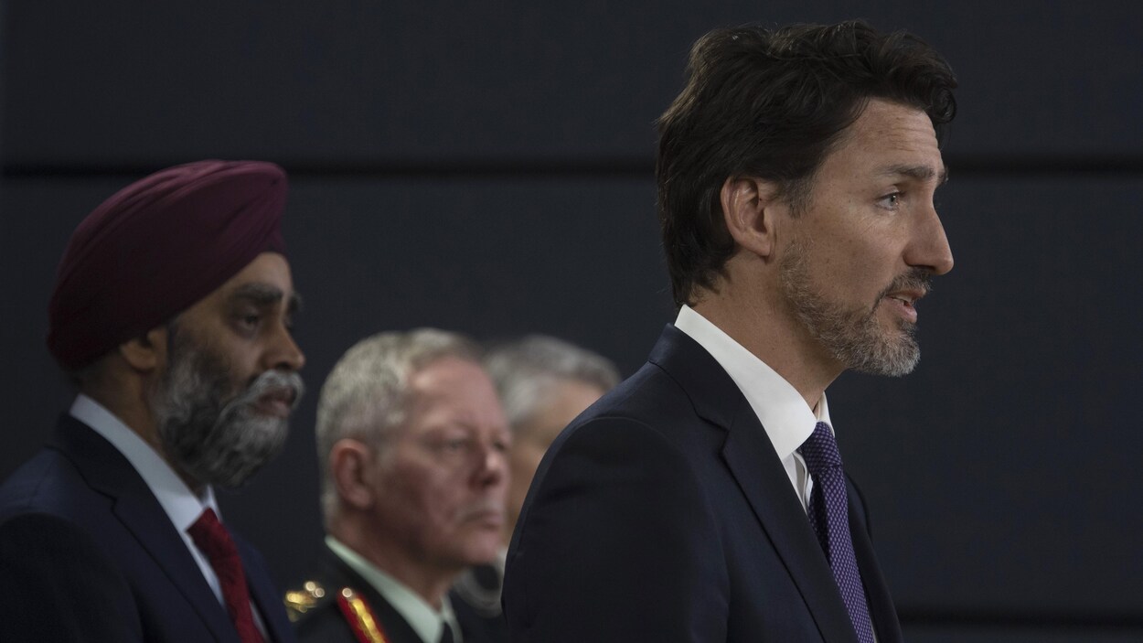 Justin Trudeau s'adresse aux médias. Derrière lui se tiennent le général Jonathan Vance et le ministre de la Défense nationale Harjit Sajjan.
