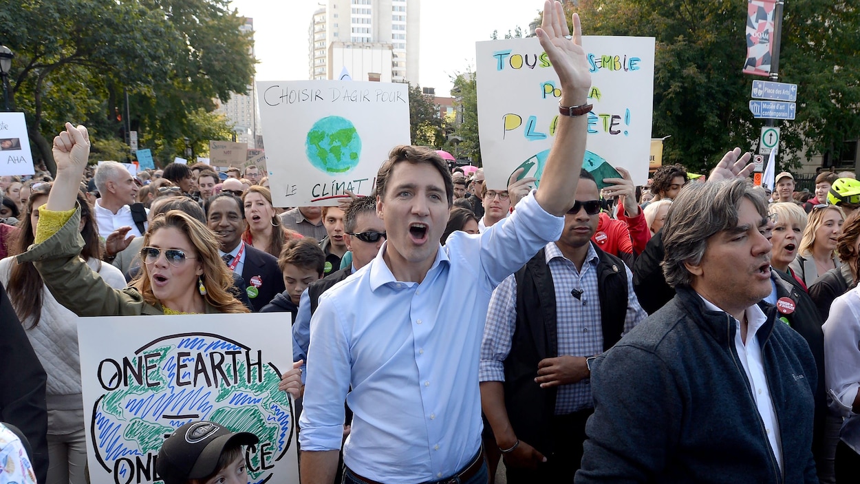 Justin Trudeau et sa femme Sophie Grégoire-Trudeau marchent devant plusieurs manifestants.