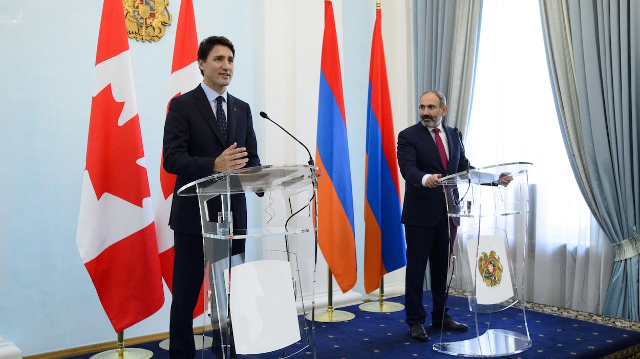 Sur une estrade, le premier ministre du Canada, Justin Trudeau, parle au micro. À ses côtés son homologue arménien, Nikol Pashinyan, le regarde et l'écoute. Derrière les deux hommes se trouvent un drapeau de chaque pays. 