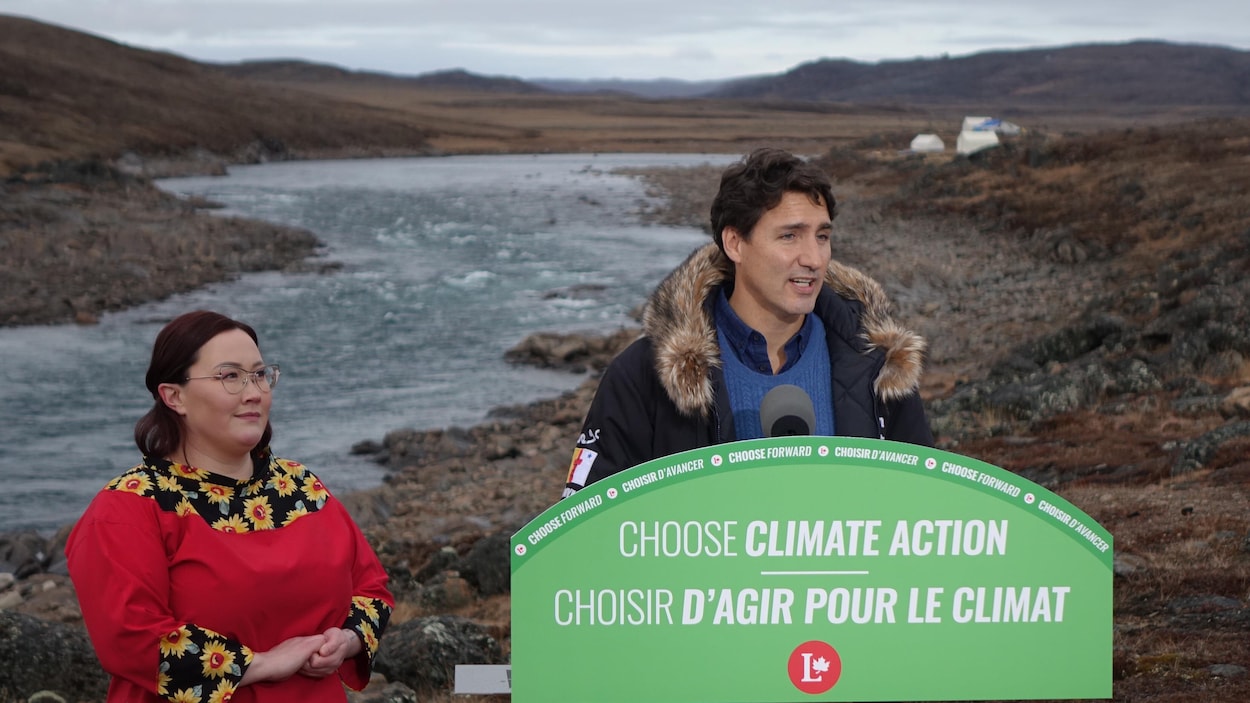Justin Trudeau donne une conférence de presse à l'extérieur avec sa candidate locale. Derrière eux coule une rivière.