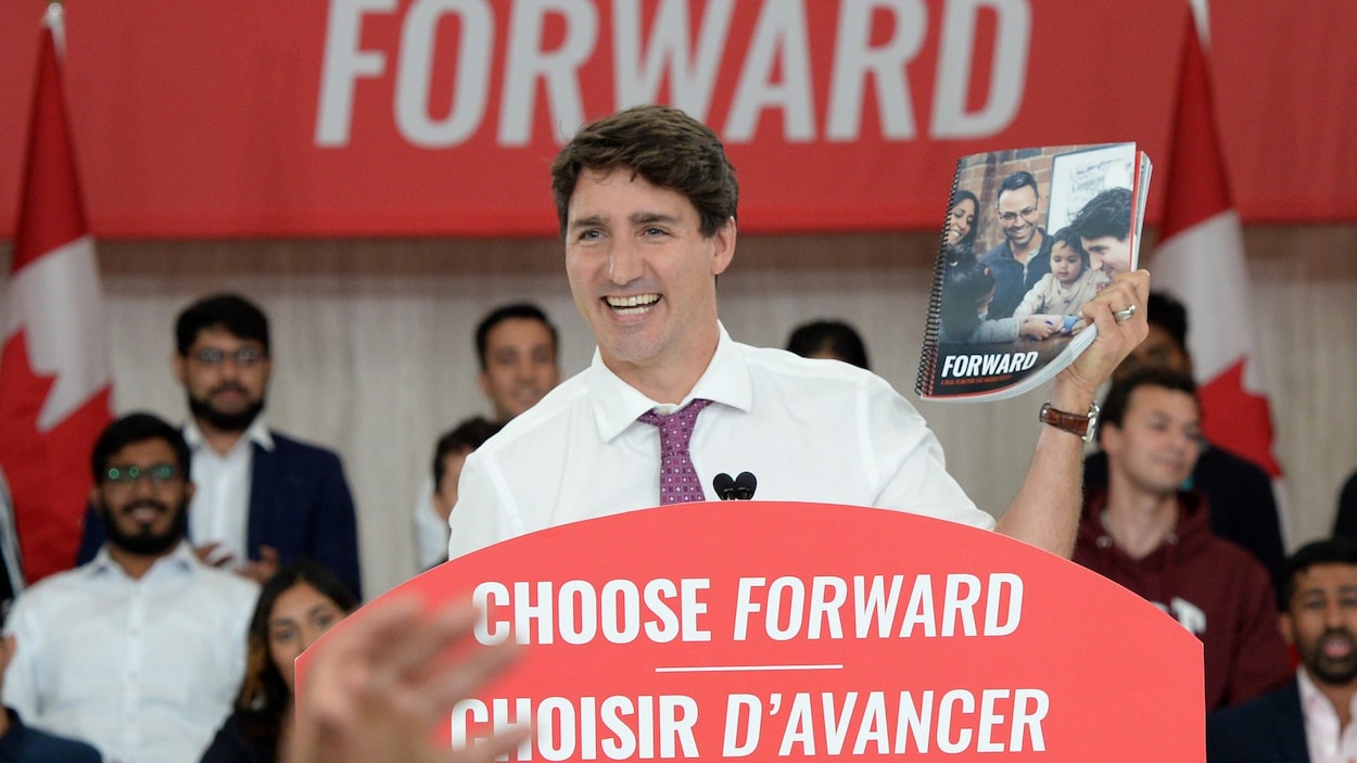 Justin Trudeau sourit. Il tient dans sa main gauche un exemplaire de la plateforme du Parti libéral du Canada.