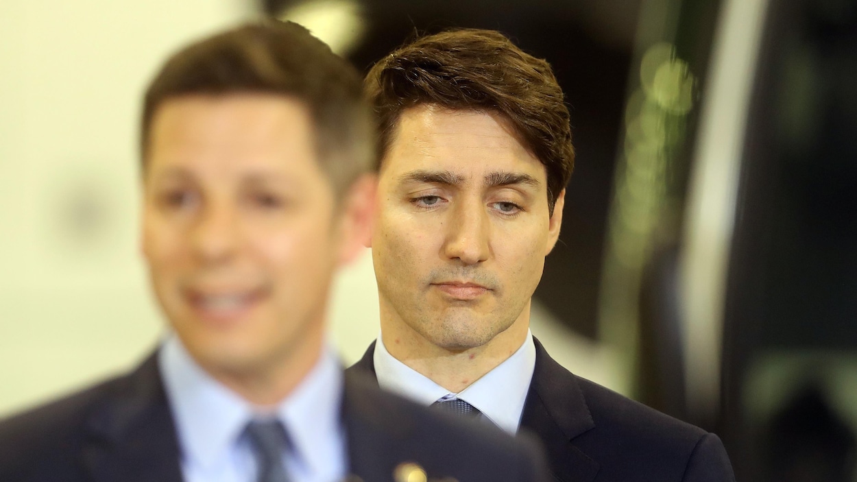 Justin Trudeau, l'air sérieux, en arrière-plan lors d'un point de presse.