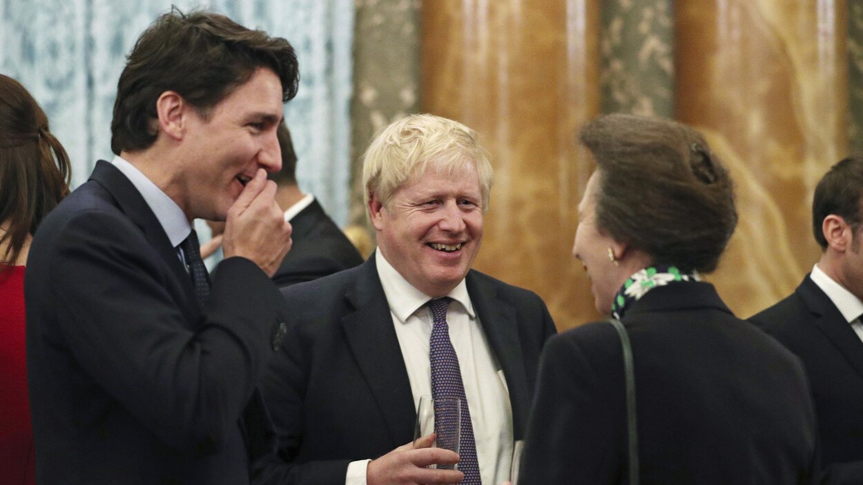 Justin Trudeau rigole avec la main devant la bouche, alors que Boris Johnson esquisse un large sourire.