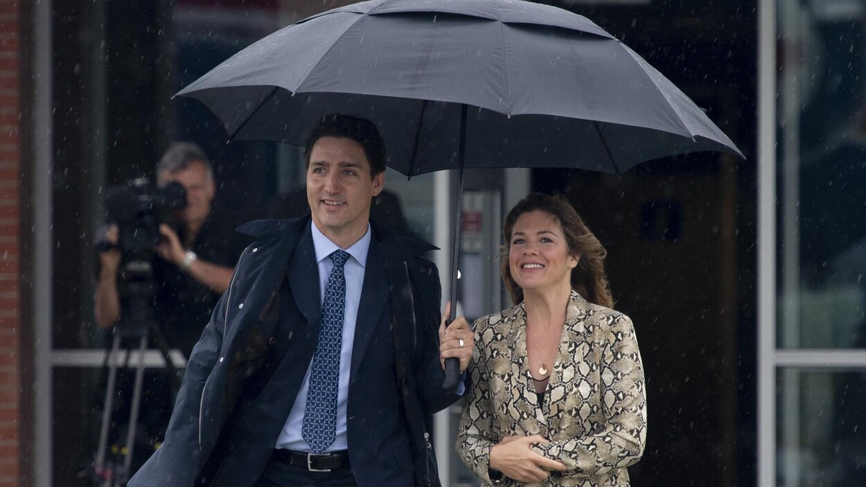 M. Trudeau tient un parapluie pour protéger le couple de la pluie.