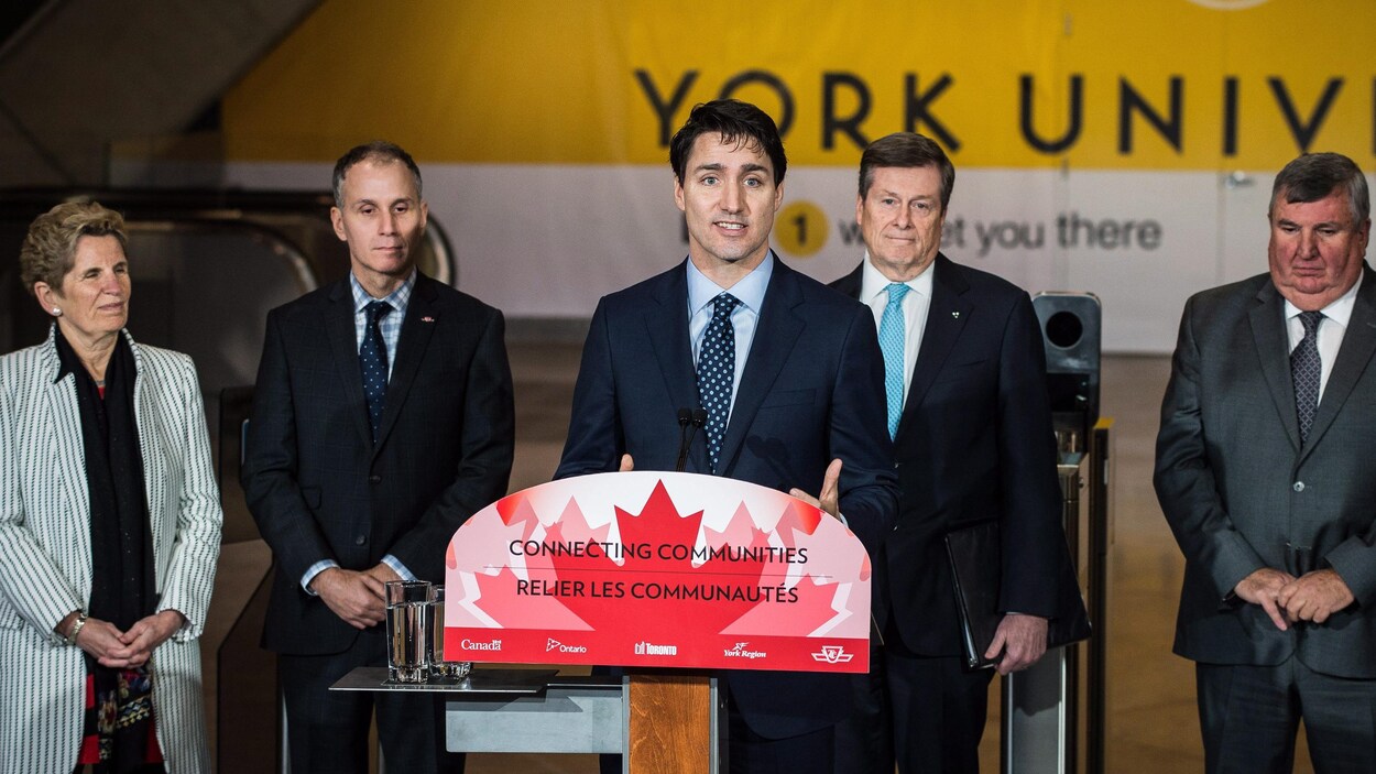 Justin Trudeau au micro entouré de Kathleen Wynne et d'autres personnes