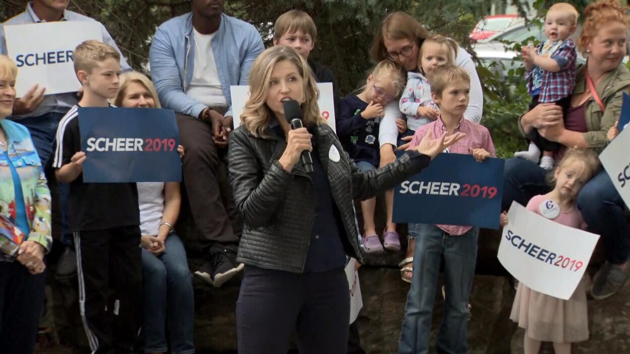 Une femme parle au micro devant une foule de partisans conservateurs. Derrière elle, des enfants tiennent des pancartes où il est écrit « Scheer 2019 ».