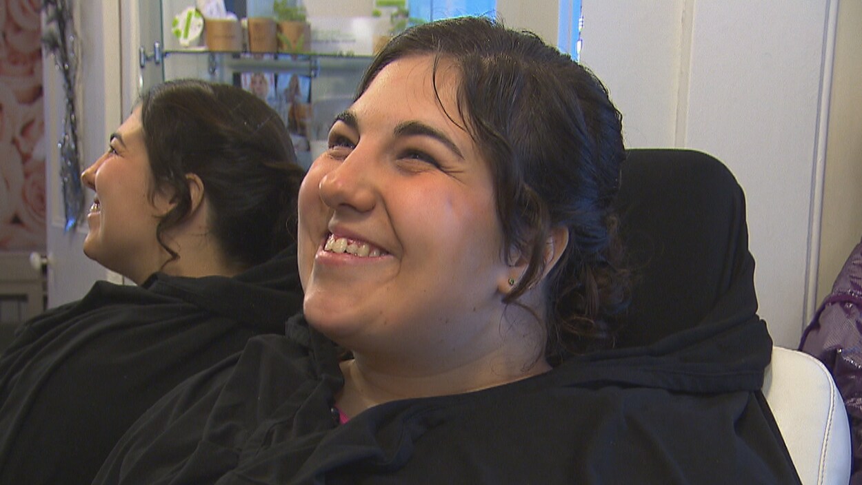 Une jeune femme aux cheveux bruns noués en chignon sourit.