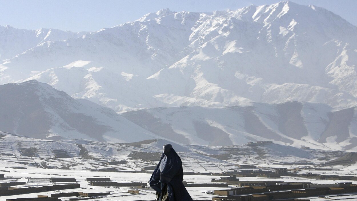 Une femme en burqa se déplace devant de majestueuses montagnes.