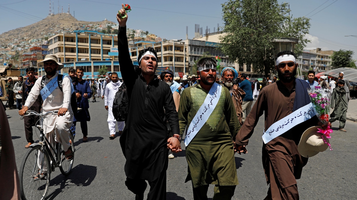 Trois hommes se tiennent par la main en tête d'un groupe de marcheurs. 