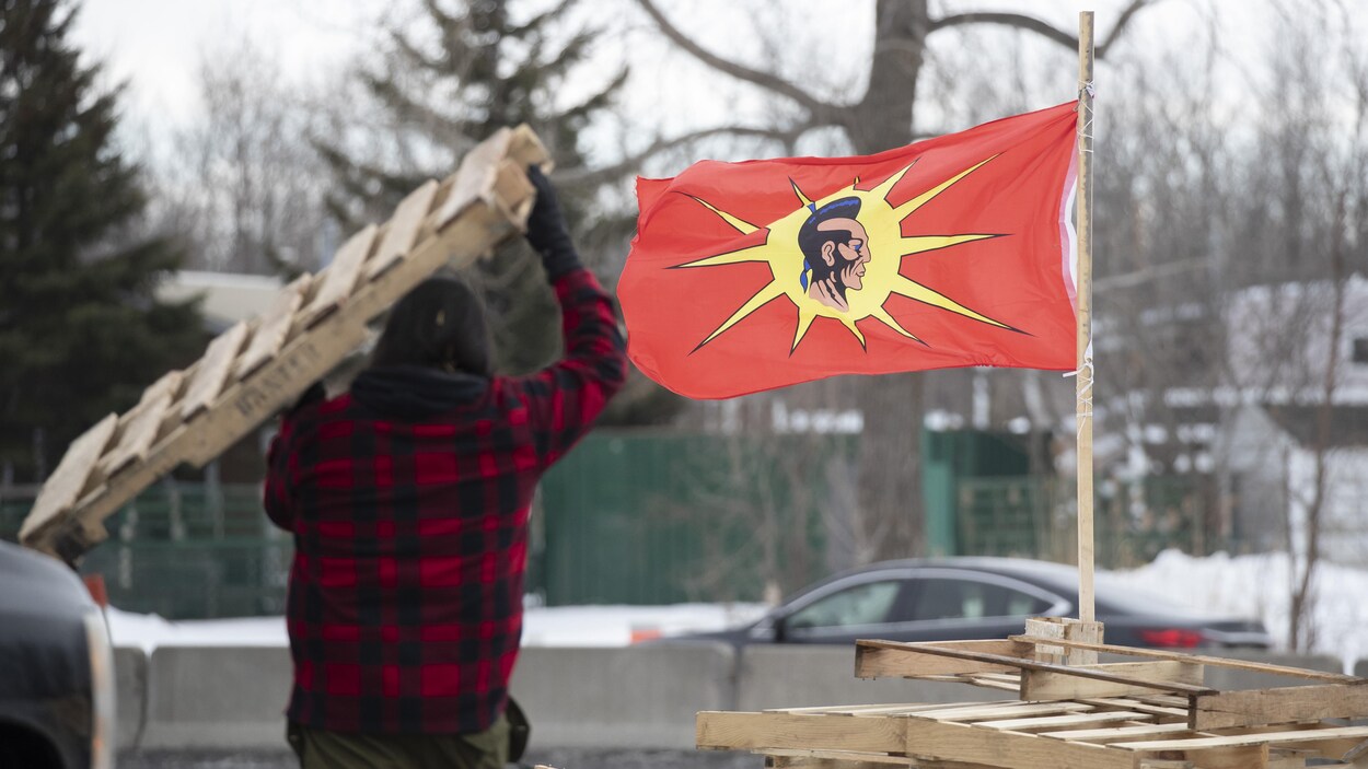 Un homme transporte une palette de bois, un drapeau mohawk flotte tout près.