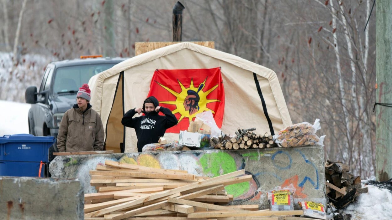 Des Autochtones derrière des planches de bois et des murets de béton constituant une barricade.